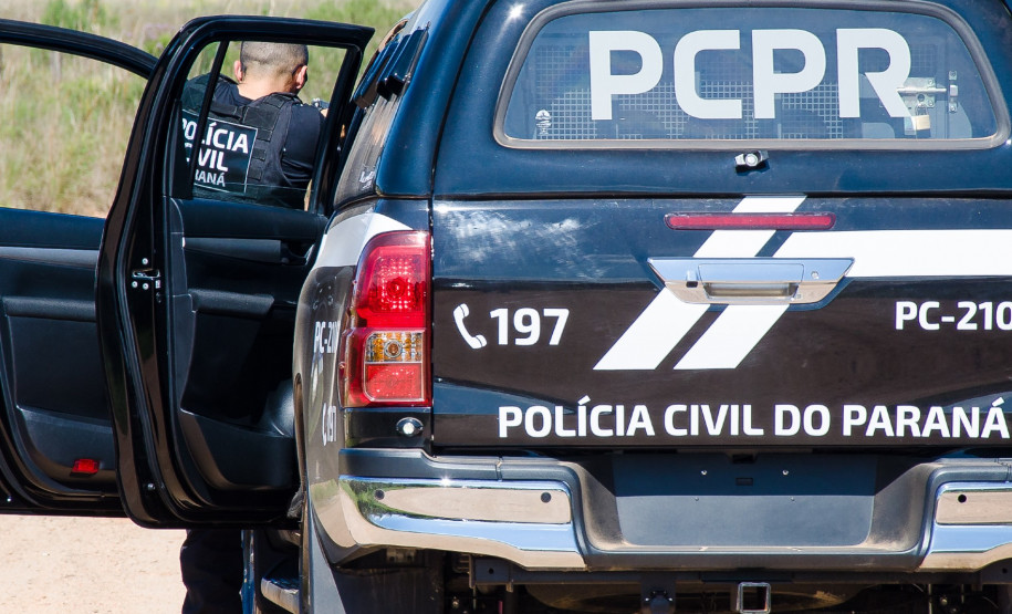 Policial civil ao lado de viatura apontando arma para suspeito