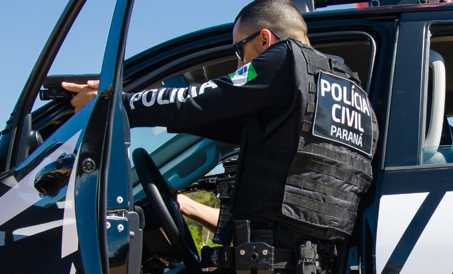 Policial civil apontando arma ao lado de viatura