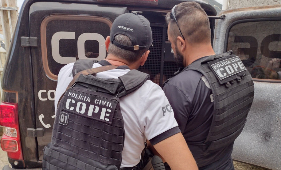 Dois policiais civis ao lado de viatura