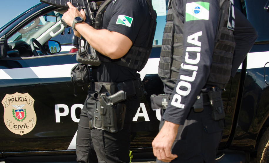 Dois policiais civis ao lado de viatura