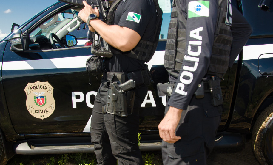 Dois policiais civis ao lado de viatura