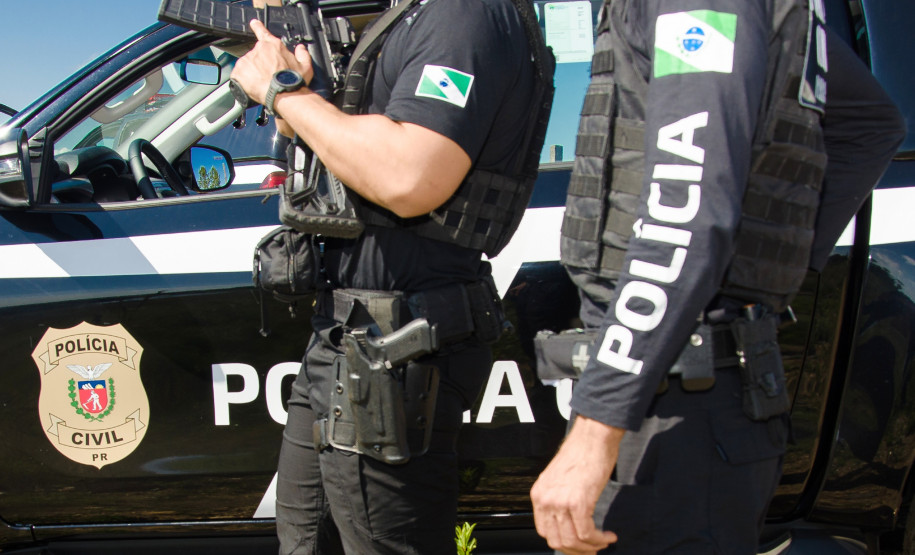 Dois policiais civis ao lado de viatura