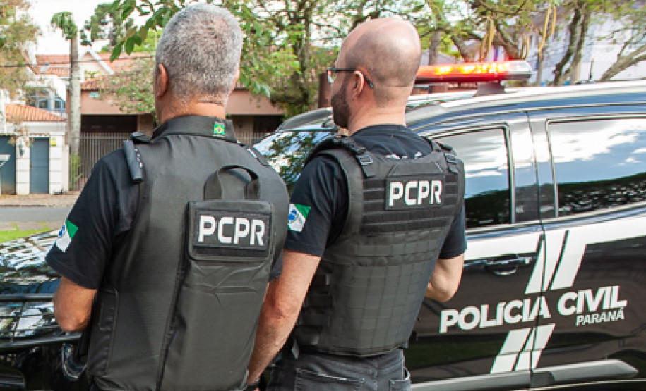 Dois policiais civis ao lado de viatura