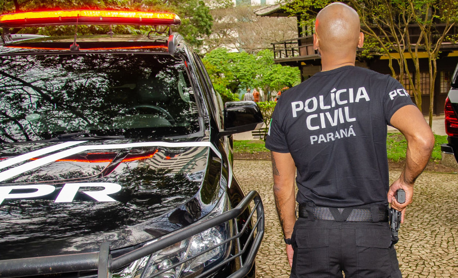 Policial civil empunhando arma ao lado de viatura