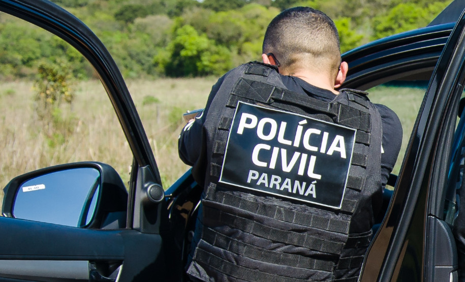 Policial civil apontando arma ao lado de viatura
