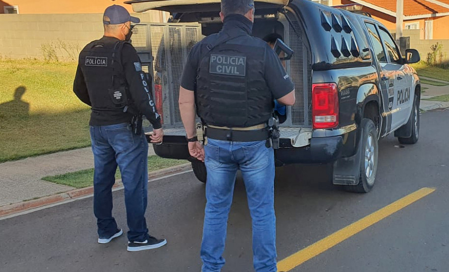 Dois policiais civis ao lado de viatura