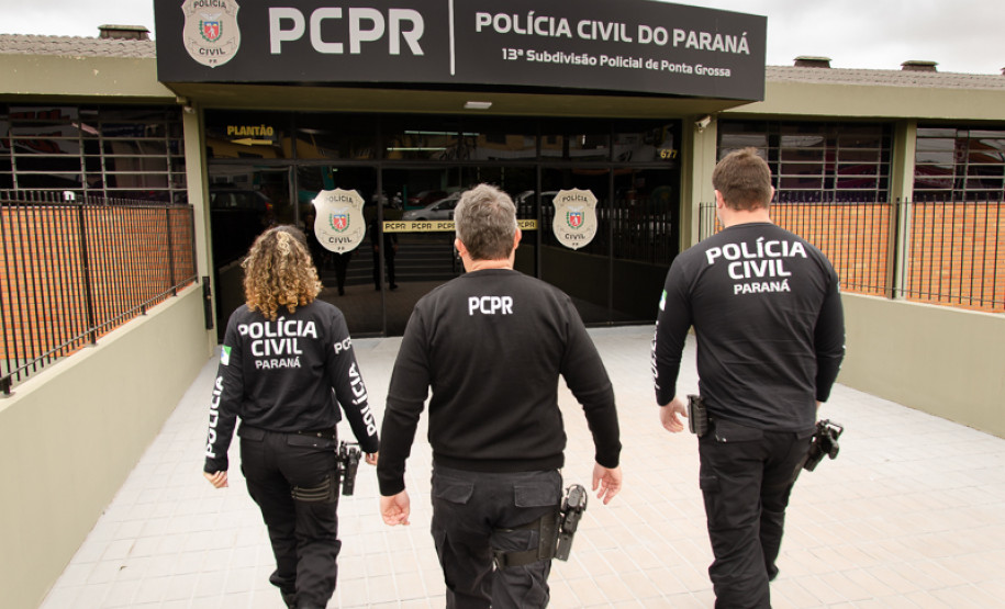 Três policiais civis de costas entrando em delegacia