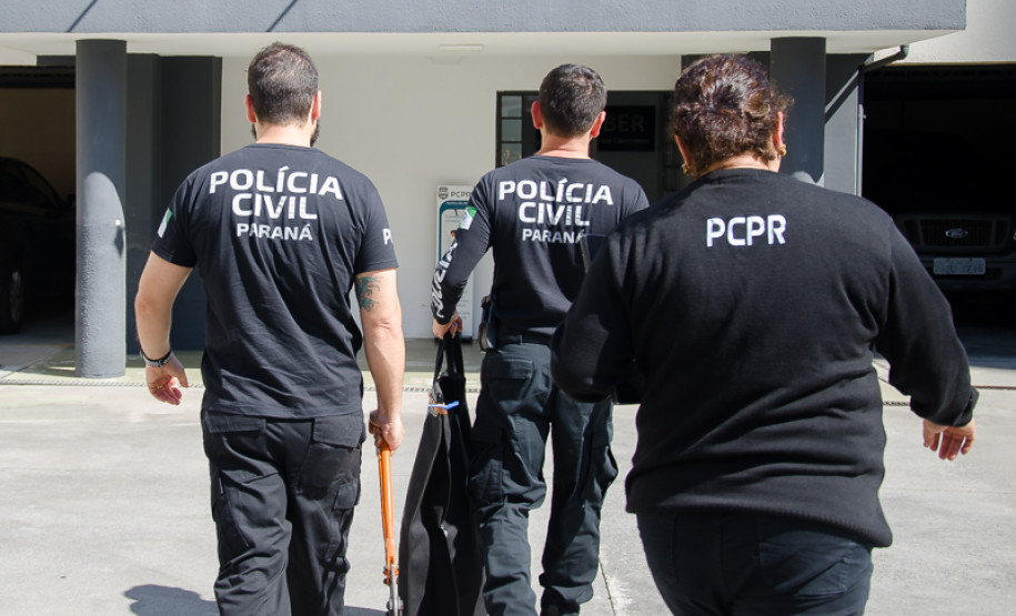 Três policiais civis de costas entrando em delegacia