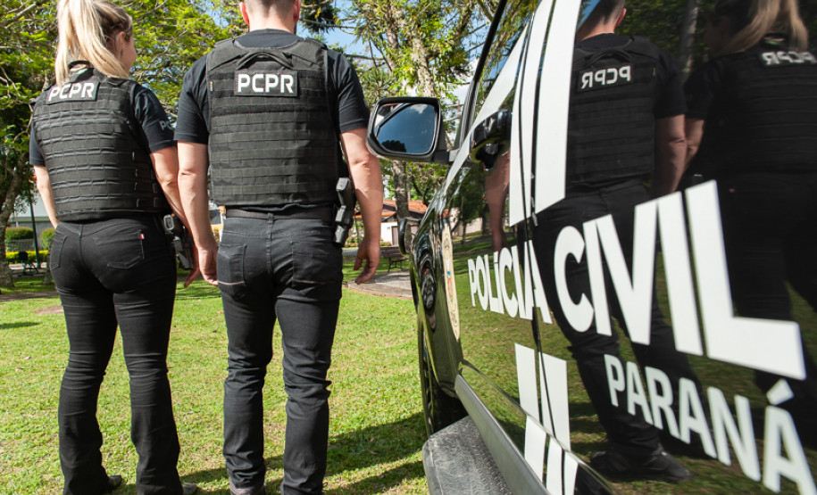 Dois policiais civis ao lado de viatura