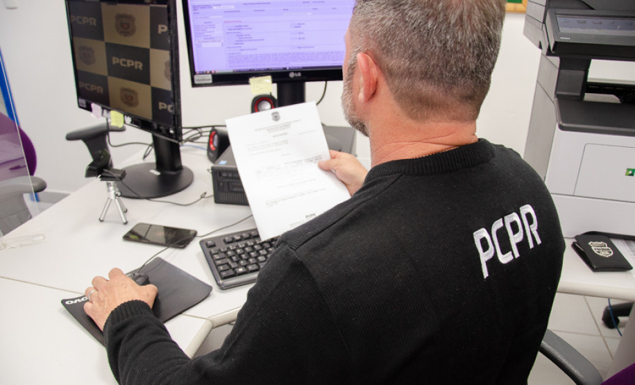 Policial civil ao computador observa documento