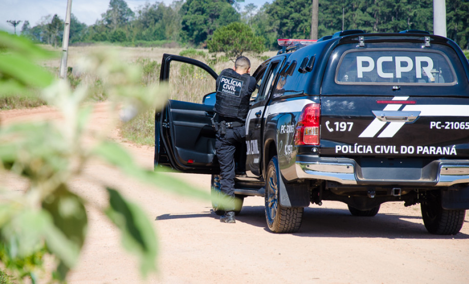 Policial civil apontando arma ao lado de viatura