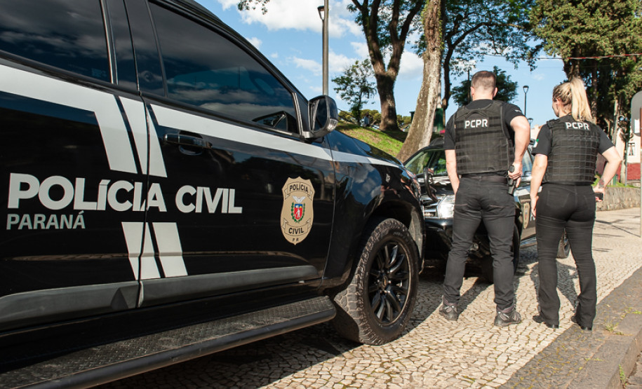 Dois policiais civis ao lado de viatura
