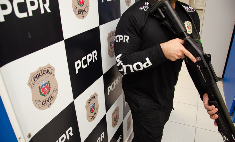 Policial civil empunha arma em frente a banner da PCPR