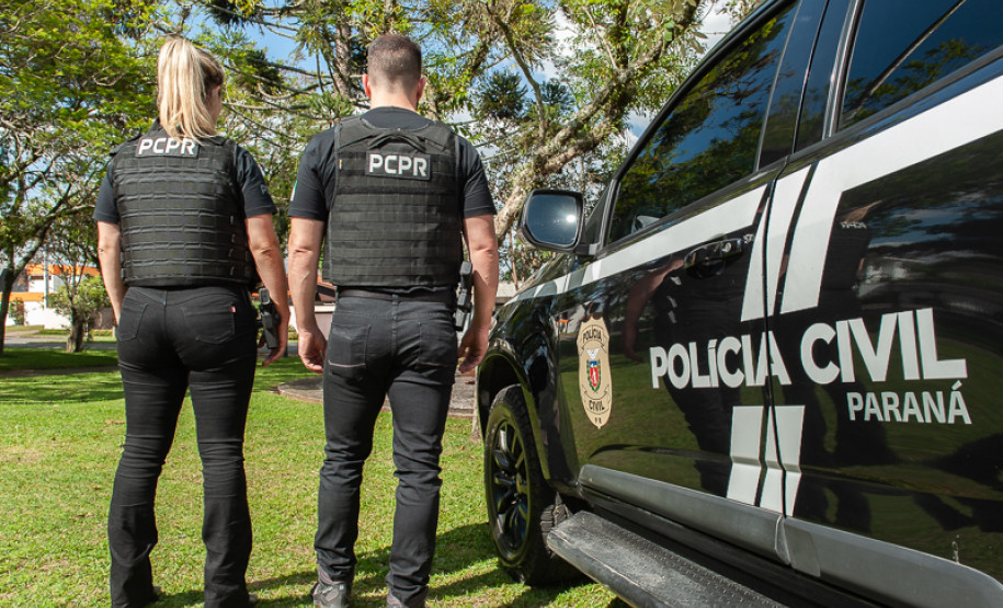 Dois policiais civis ao lado de viatura