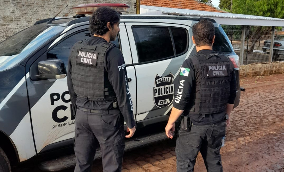 Dois policiais civis ao lado de viatura