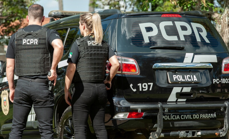 Dois policiais civis ao lado de viatura