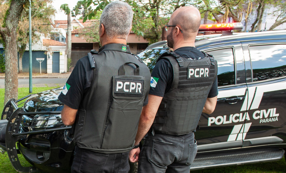 Dois policiais de costas ao lado de viatura